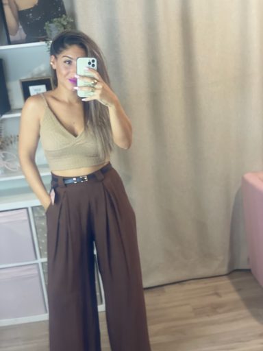 Mujer sonriendo en un espejo, con top beige y pantalones anchos marrones.